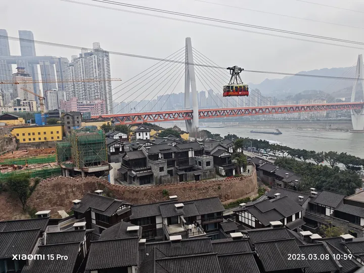 索道缆车经过跨江桥前，近处是层叠传统屋顶